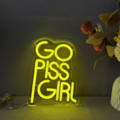 a neon sign with the words go piss girl on it next to flowers and a vase