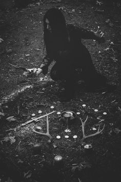 a woman kneeling on the ground in front of some candles and deer antlers,