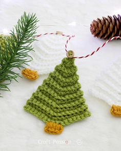 a crocheted christmas tree ornament next to a pine cone on a white surface