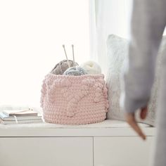 a knitted basket sitting on top of a white shelf next to a window sill