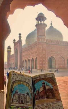 an open book sitting on top of a wooden table next to a building with domes