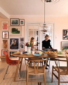 two women sitting at a wooden table in a room with pictures on the wall and wood floors