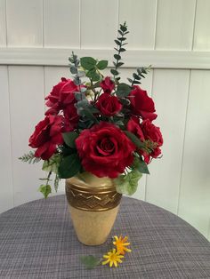 a vase filled with red roses sitting on top of a table next to a yellow flower