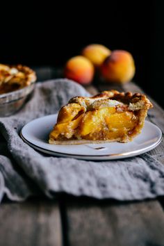 a slice of peach pie on a white plate next to some peaches in the background