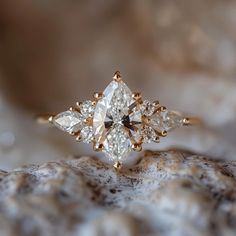 an engagement ring with three pear shaped diamonds on top of it, sitting on a rock