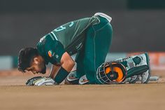 a man in green shirt and white gloves on ground with baseball glove next to him