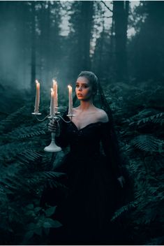 a woman holding two candles in the woods