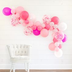 a white chair sitting in front of a wall with pink and red balloons on it