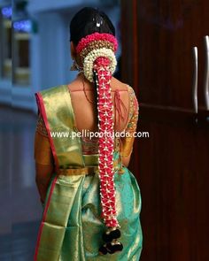 the back of a woman's head wearing a green and pink saree with flowers in her hair