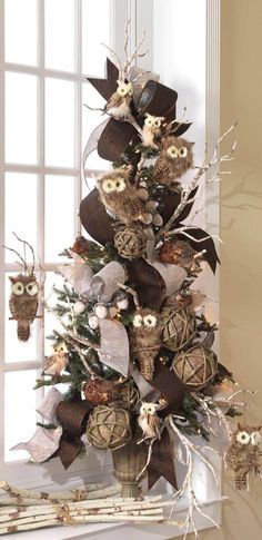 a decorated christmas tree with owls and pine cones on the top is in front of a window