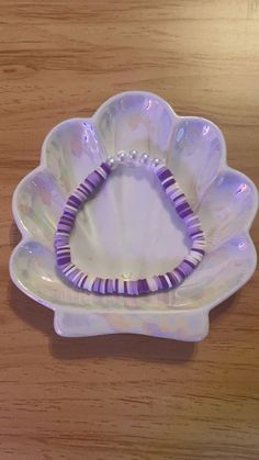 a purple beaded bracelet sitting on top of a white flower shaped bowl with beads