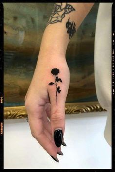 a woman's hand with a black flower tattoo on her left thumb and finger