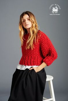 a woman sitting on a stool wearing a red sweater