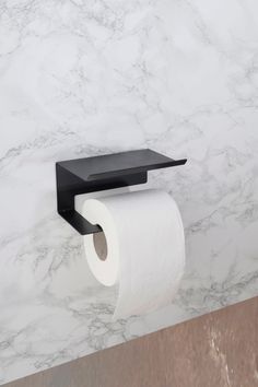 a black toilet paper holder mounted on a marble wall next to a roll of toilet paper