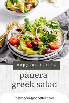 a white plate topped with a salad next to a fork and bowl filled with lettuce