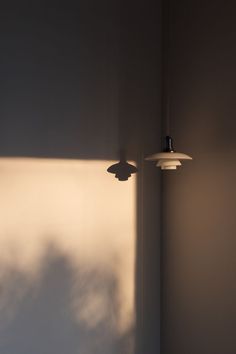 two lamps are hanging in the corner of a room with white walls and shadows on the wall