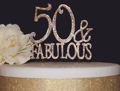 a 50th birthday cake topper with the number 50 and fabulous written on it next to a flower