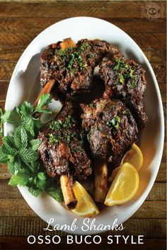 lamb shanks with lemon wedges and parsley on a white plate over a wooden table