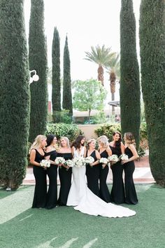 a group of women standing next to each other in front of some tall trees and bushes