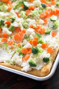 a pizza with carrots, broccoli and cauliflower on it sitting on a table