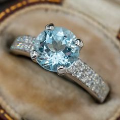 This pretty ring is centered with one (1) round modified brilliant cut natural aquamarine weighing 1.51 carats that is set into a four-prong setting. The shoulders of the ring are each accented with two-rows of eight (8), bead set, round brilliant cut diamonds. The side faces of the head are each accented with thirteen (13), bead set, round brilliant cut diamonds. The ring measures 8.1mm at the top, rises 8.1mm above the finger, tapering to 2.6mm wide and 1.1mm thick at the base of the shank. This ring is currently a size 6.25. Aquamarine Stone Ring, Aquamarine Cocktail Ring, Aquamarine Ring Vintage, Birthstone Engagement Rings, Princess Jewelry, Multicolor Jewelry, Aquamarine Jewelry, Aquamarine Stone, Aquamarine Rings