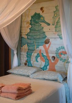 a bed with white sheets and seahorses painted on the wall next to it