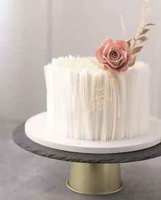 a cake with white frosting and a pink flower on top