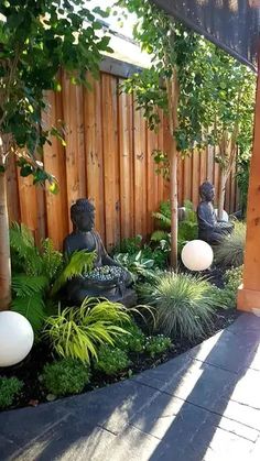 a small garden with buddha statues and plants in the center, along side a wooden fence