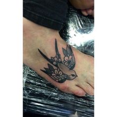 a small bird tattoo on the foot of a person's left foot with flowers around it