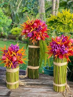 three bamboo vases with flowers in them on a wooden table next to some plants