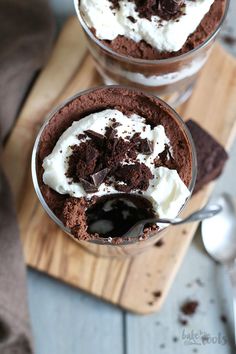 two desserts with chocolate and whipped cream in glasses on a cutting board next to spoons