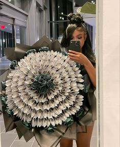 a woman taking a selfie in front of a giant paper flower arrangement with her cell phone