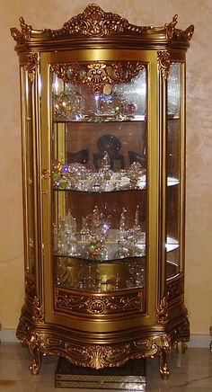 an ornate display case with many glass items on the top and bottom shelves in gold