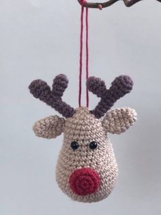 a crocheted reindeer ornament hanging from a tree branch with red nose