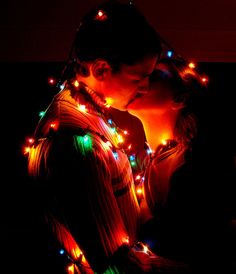 a man and woman standing next to each other with christmas lights all over their body