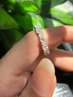 a woman's hand holding a diamond ring in front of a green potted plant