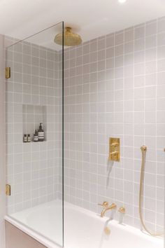 a bathroom with white tile and gold fixtures on the shower head, tub, and wall