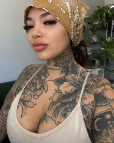 a woman with tattoos on her chest wearing a white tank top and brown bandana