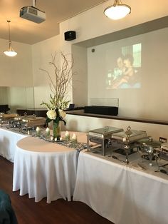 a long table is set up with white linens and flowers in front of a projector screen