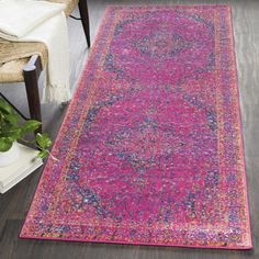 a pink and blue rug on the floor next to a chair with a plant in it