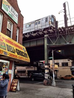 the train is going over the bridge and people are standing on the sidewalk near it