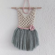 a crocheted top hanging on a wall with a flower in the center and a wooden hanger attached to it