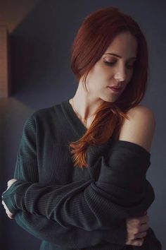 a woman with red hair wearing a green sweater and looking off to the side while leaning against a wall