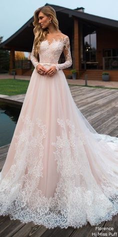 a woman standing on a dock wearing a wedding dress with long sleeves and lace detailing