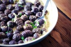 a bowl filled with some kind of food on top of a wooden table next to a spoon