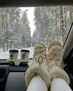 someone's feet in the passenger seat of a car with snow covered trees behind them