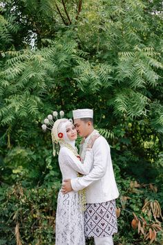 a man and woman dressed in traditional thai garb standing next to each other near some trees