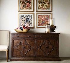 a wooden cabinet sitting next to a white chair in front of pictures on the wall