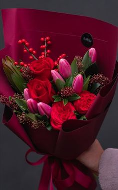 a person holding a bouquet of red and pink flowers