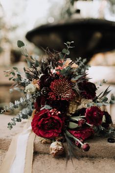 a bouquet of flowers sitting on top of a stone wall next to a fountain with greenery